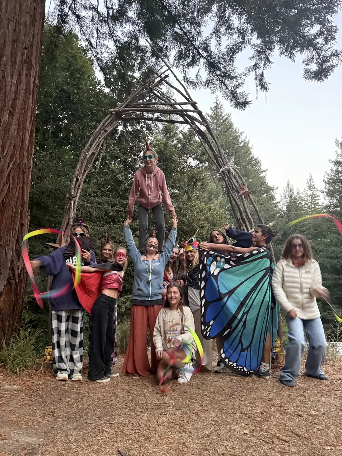 13 Moons girls and mentors laughing beneath a woven arch of branches in the redwoods